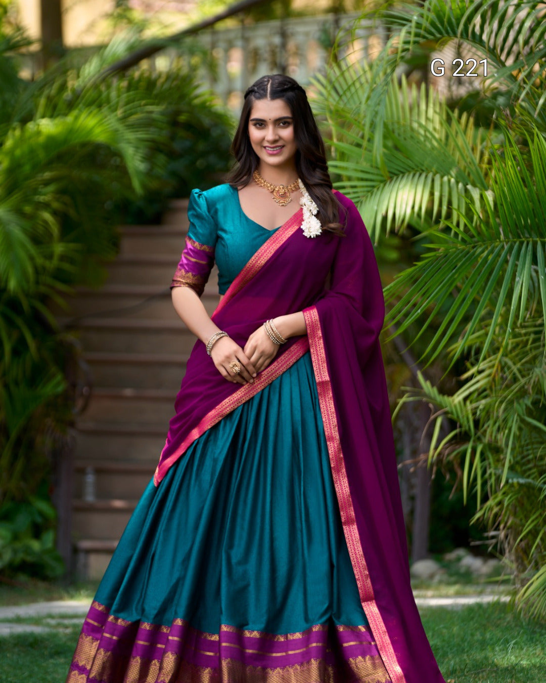 Woman wearing a teal and purple saree with a green outdoor background