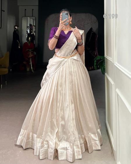 Person wearing a white saree with a purple blouse in a room.