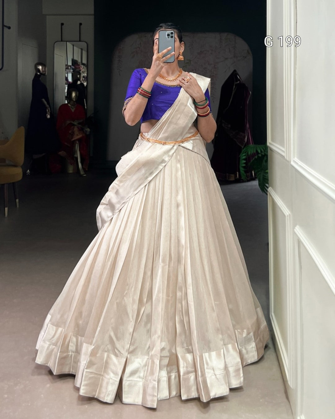 Person wearing a traditional outfit with a blue top and white saree in a room.