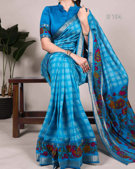 Woman wearing a blue saree with floral patterns, standing against a neutral background.