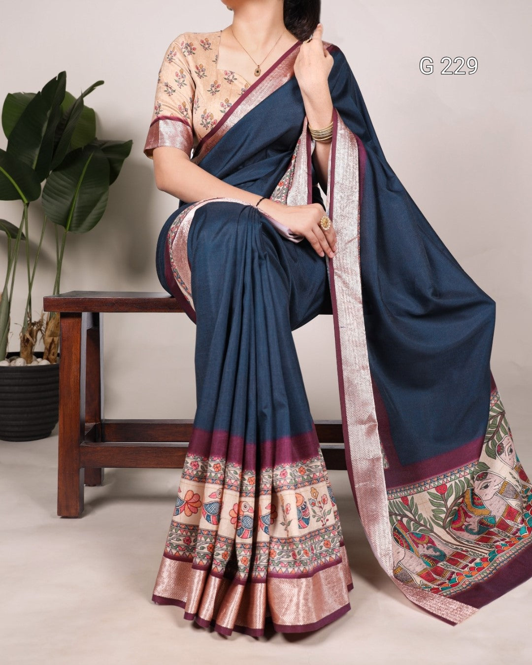 Woman wearing a blue saree with floral patterns, sitting on a wooden stool.