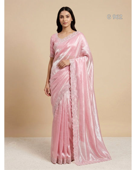 A woman modeling a light pink silk saree with a matching pink blouse, standing against a solid beige studio background. The saree has a subtle sheen and a scalloped lace border, with the code 'G 962' printed in the top right corner.