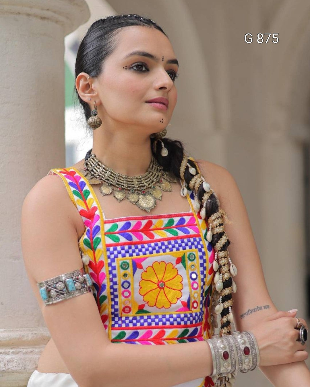Woman wearing a colorful traditional outfit with intricate jewelry against a blurred architectural background.