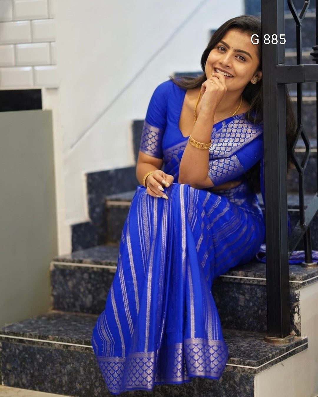 Woman in a blue saree sitting on steps indoors
