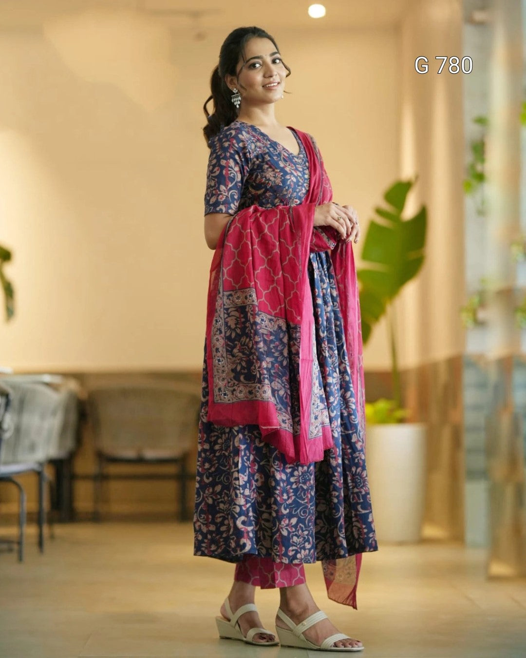 Woman wearing a traditional outfit with a pink and blue patterned dress in an indoor setting.
