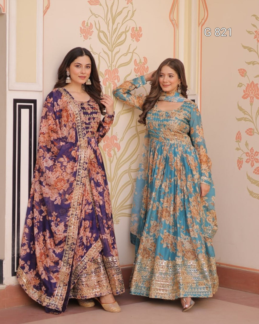 Two women in floral outfits standing against a decorative wall.