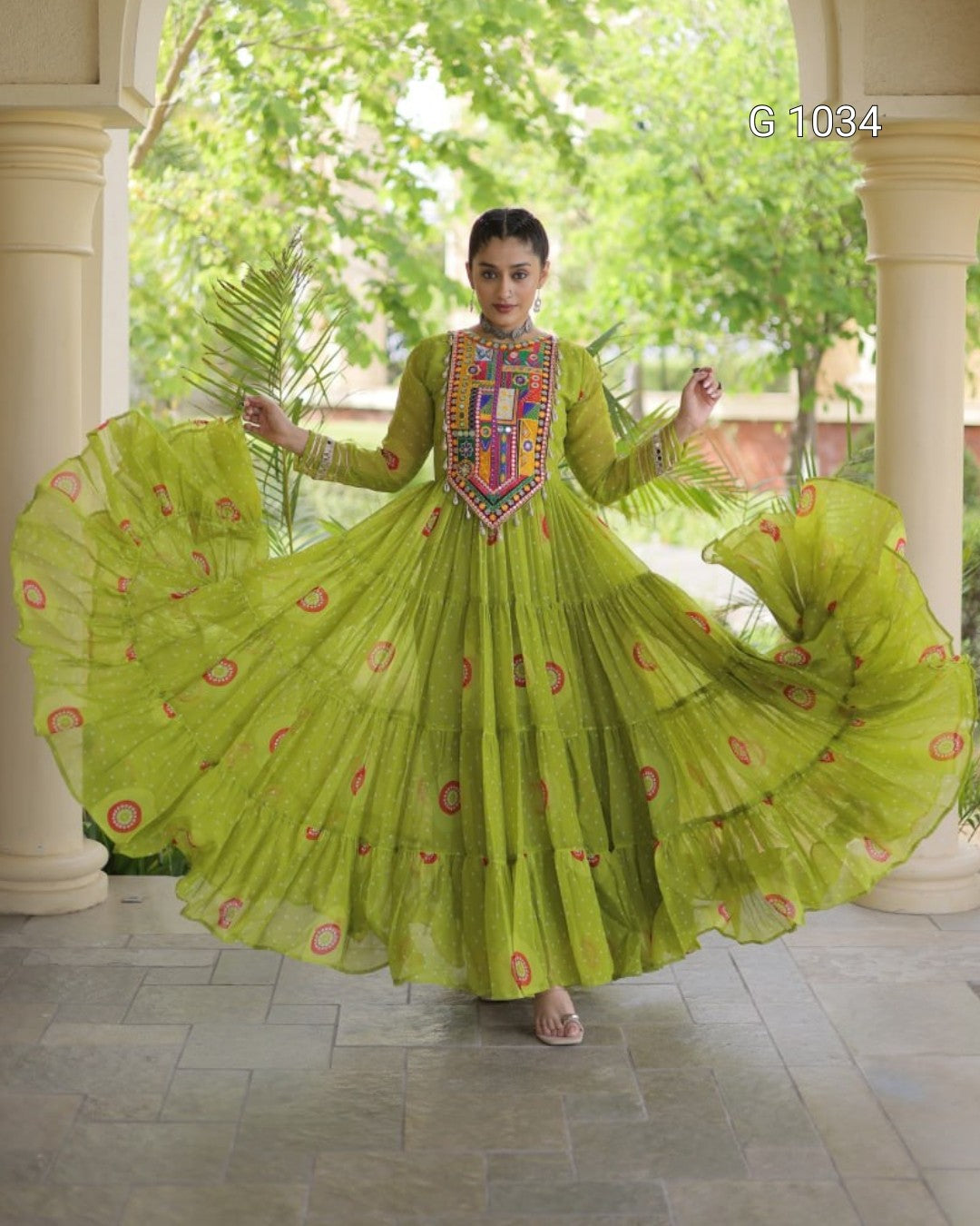 A woman wearing a bright lime green traditional Anarkali gown with a heavily embroidered neckline and red circular motifs, posing with her skirt spread wide in a courtyard.