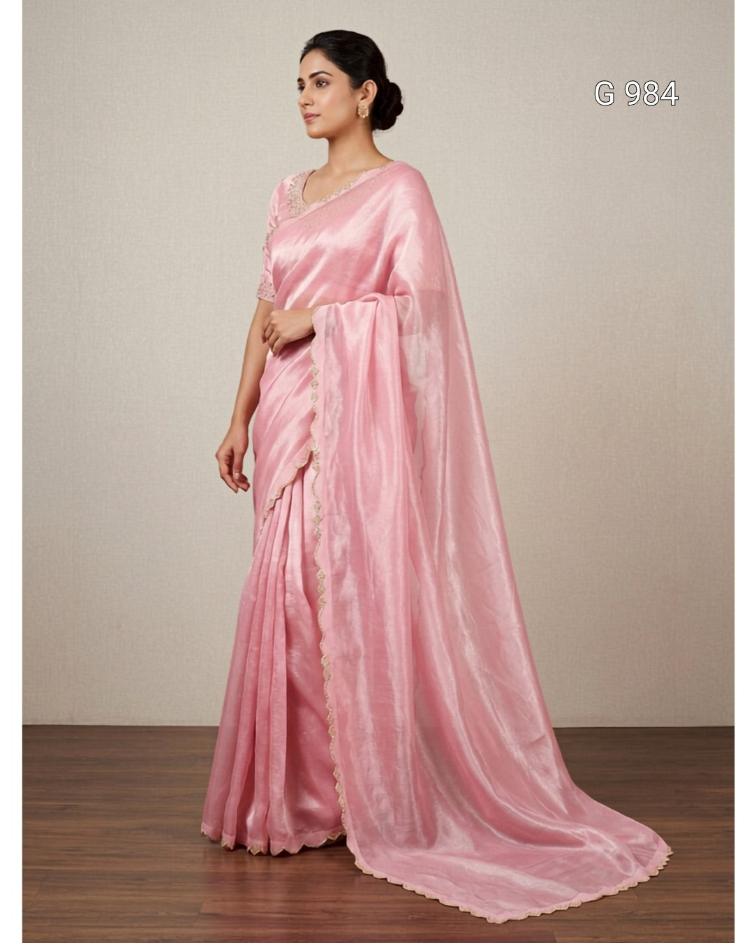 A woman modeling a light pink silk saree with a matching dupatta, standing against a neutral beige wall and wooden floor. The text 'G 984' is visible in the top right corner.