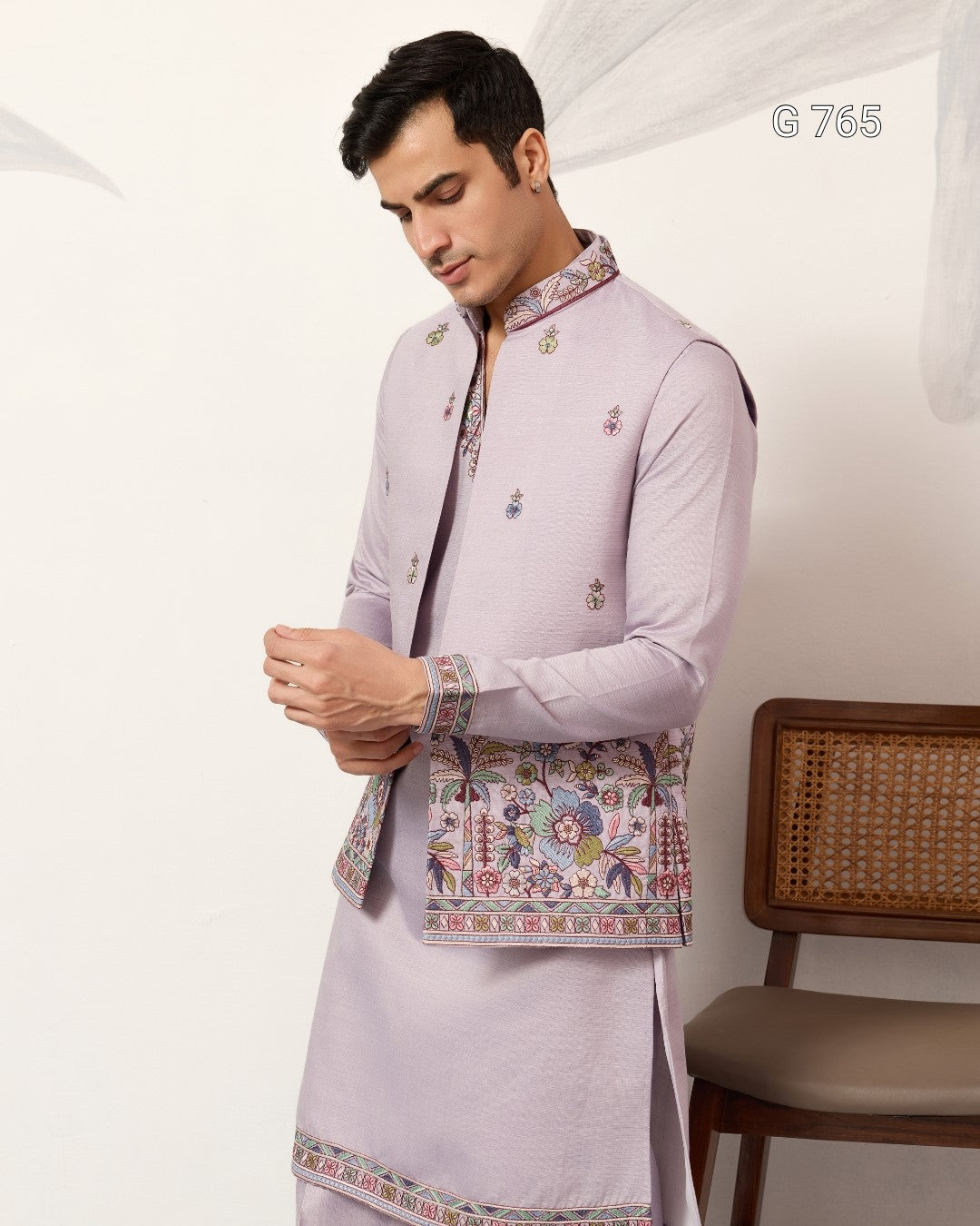 Man wearing a light purple traditional outfit with intricate patterns on a white background