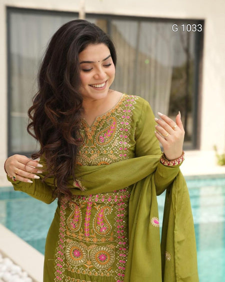 A woman wearing an olive green traditional embroidered kurta set with pink and gold detailing, standing outdoors near a swimming pool. The image includes the text 'G 1033' in the top right corner.