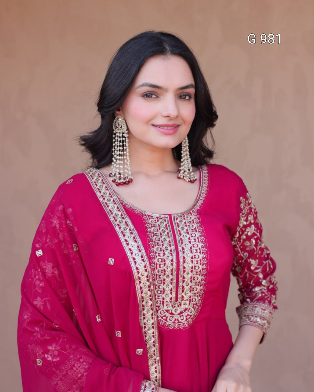 A woman modeling a bright pink traditional outfit with gold embroidery and a matching sheer dupatta, set against a plain beige background. The text 'G 981' is visible in the top right corner.