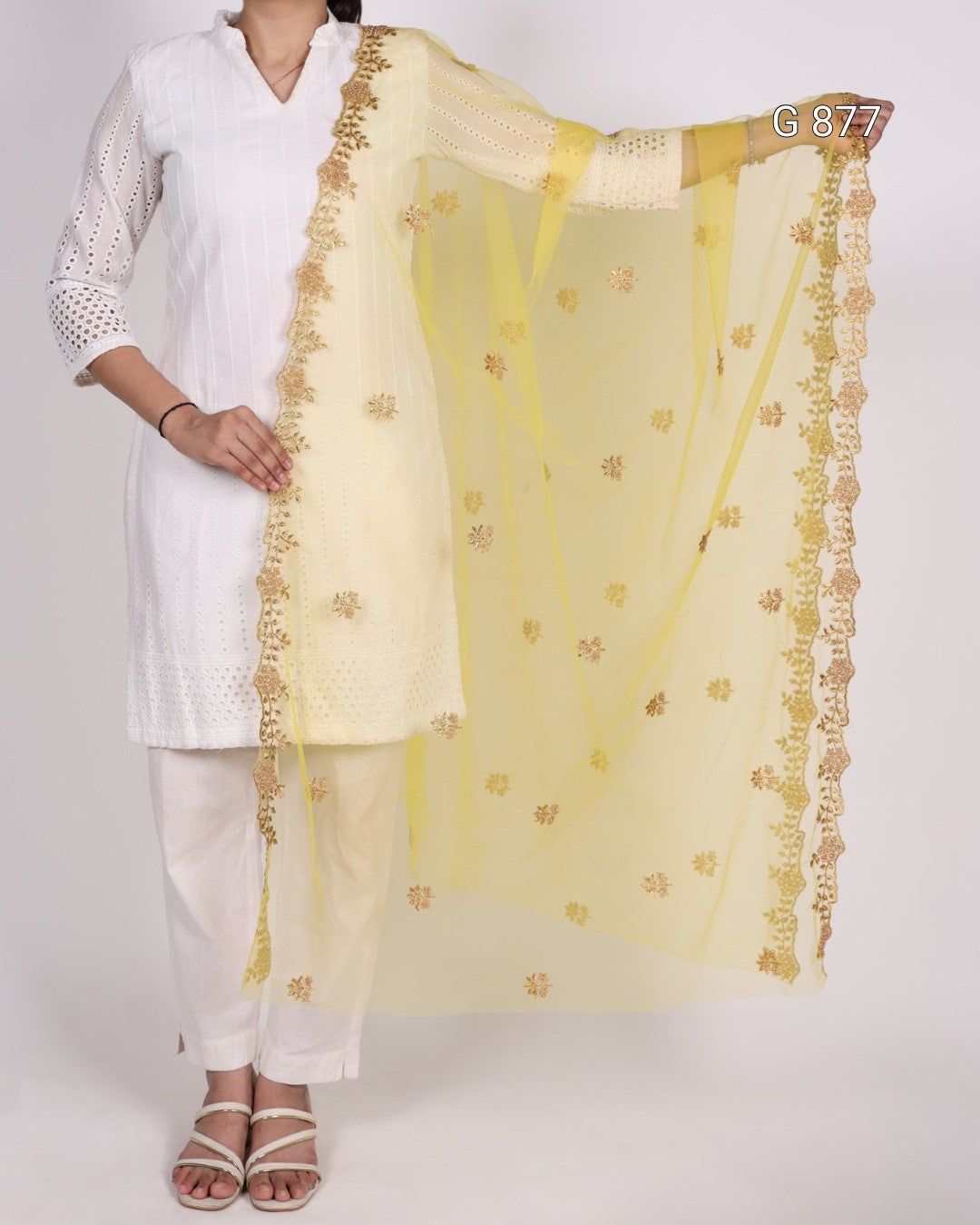 Woman wearing a white kurta with a yellow dupatta featuring gold embroidery on a plain background