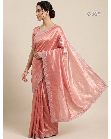 A woman modeling a shiny pink saree with a matching blouse against a plain beige studio background. The saree has a metallic sheen and a decorative border, with a small text overlay 'G 984' in the top right corner.