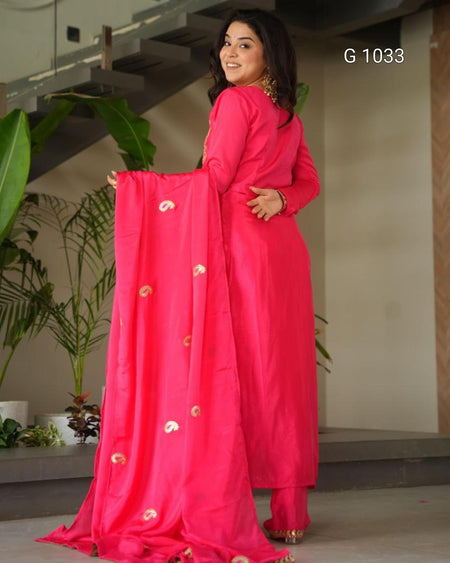 A woman modeling a bright pink traditional Indian outfit with a matching dupatta featuring small gold paisley motifs, standing indoors near plants and stairs. The text 'G 1033' appears in the top right.