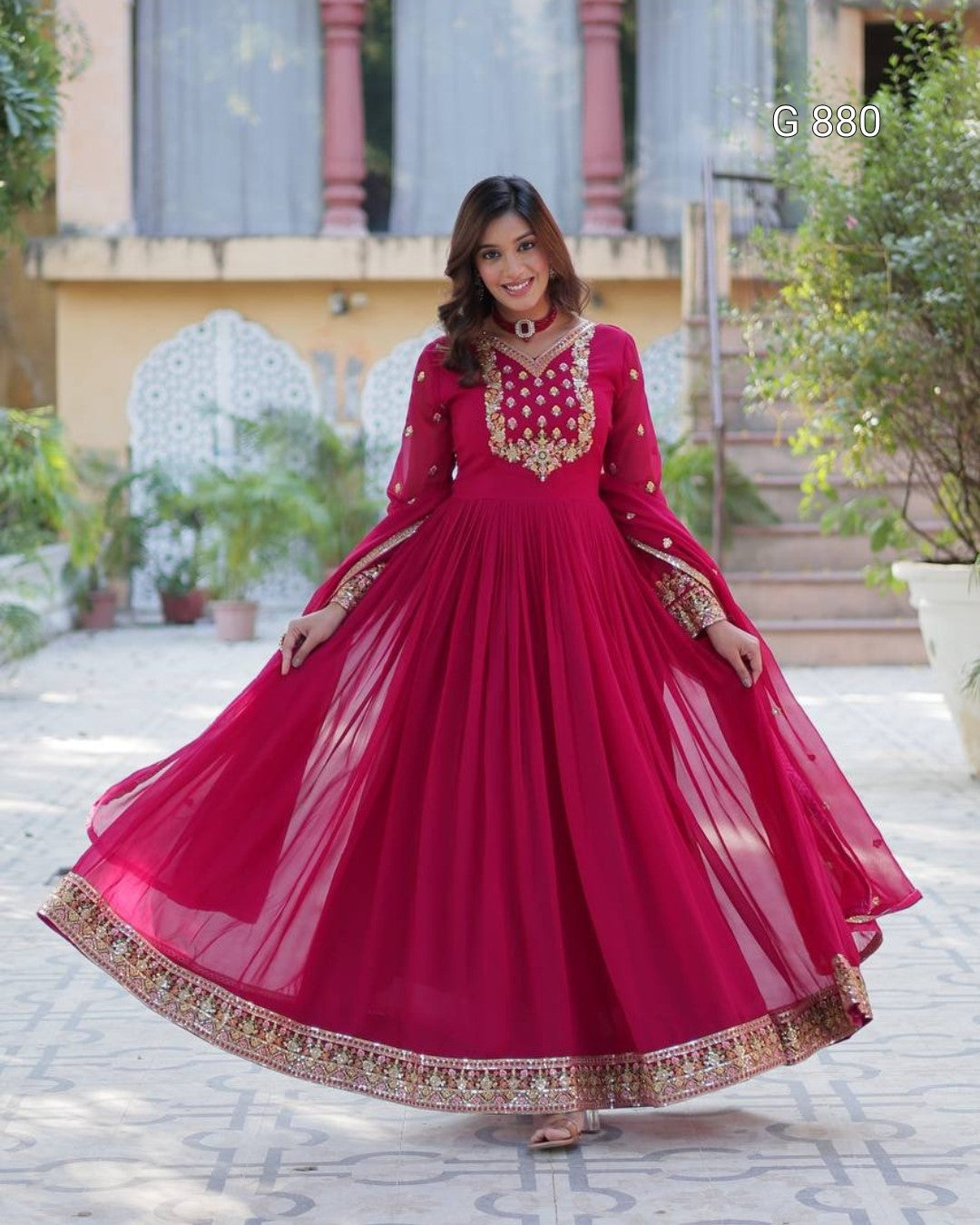 Woman in a red traditional outfit with gold embroidery standing outdoors.