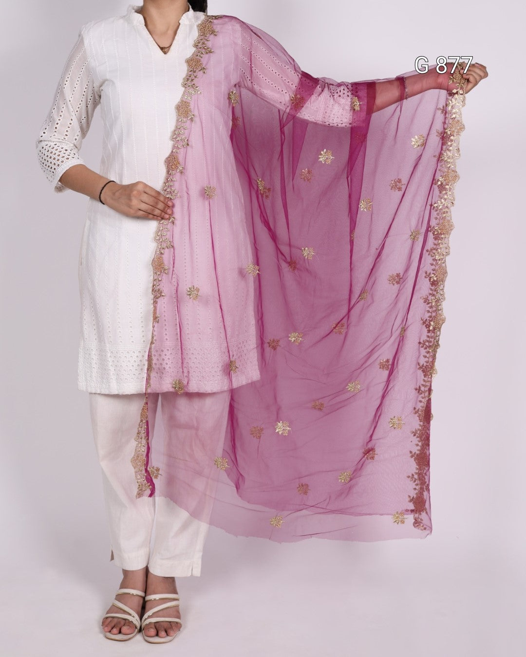 Person wearing a white outfit with a pink dupatta featuring gold embroidery on a plain background