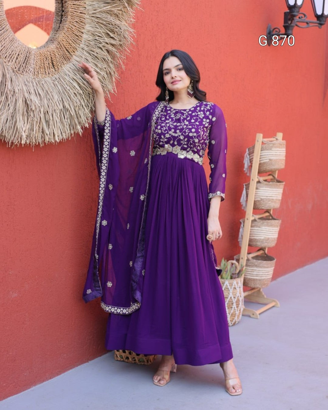 Woman in a purple dress standing against a red wall with decorative elements.
