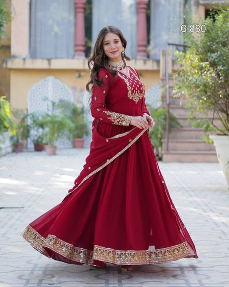 Woman in a red traditional outfit with gold embroidery standing outdoors.