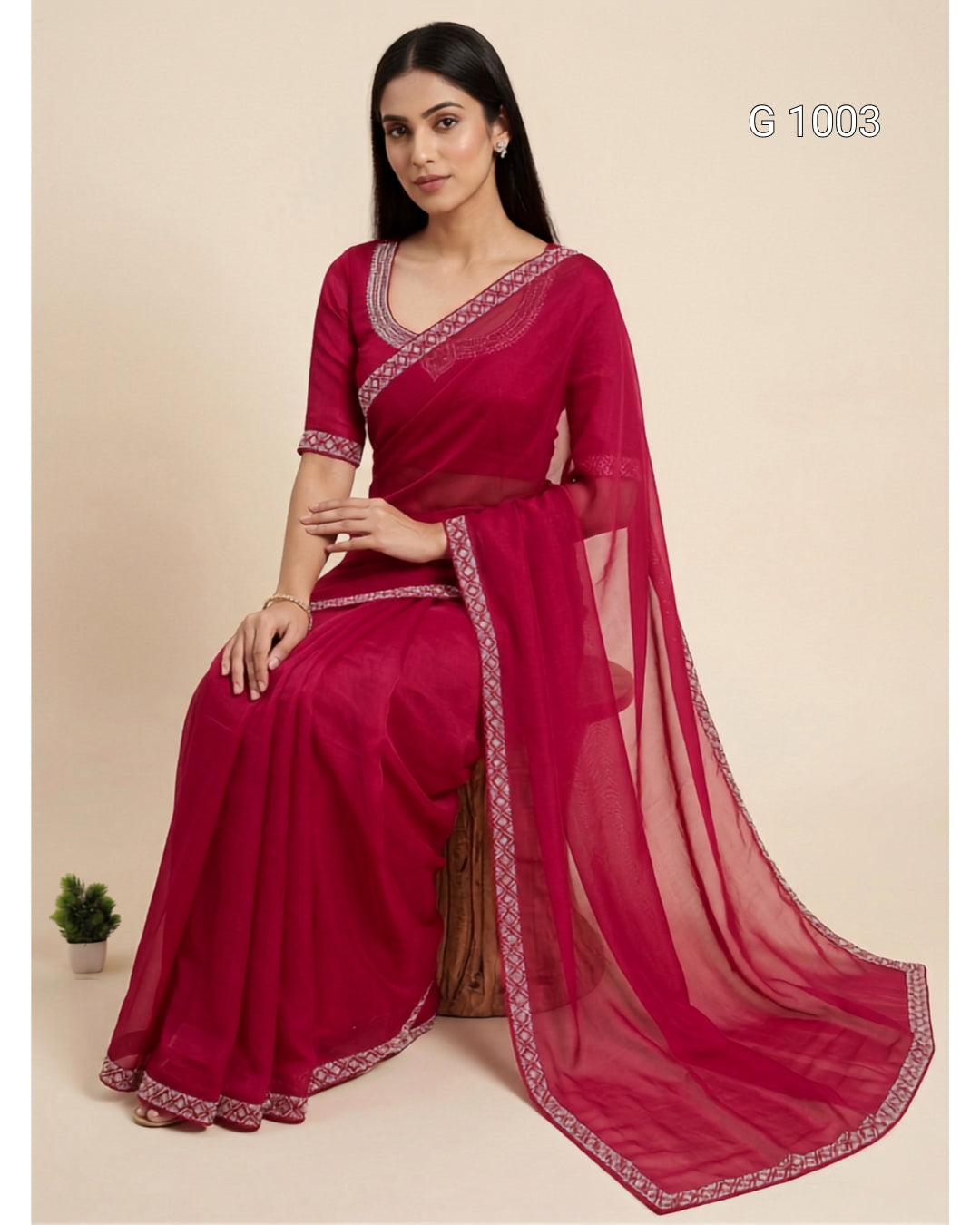 A woman models a deep magenta pink georgette saree with a matching blouse and a long sheer dupatta, both featuring silver embroidered borders. The image is set against a plain beige background with a small potted plant on the left and a style code 'G 1003' in the top right corner.