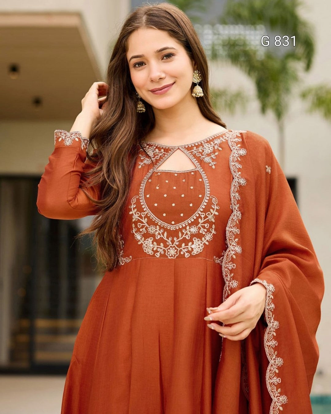 Woman wearing a rust-colored dress with intricate white embroidery outdoors.