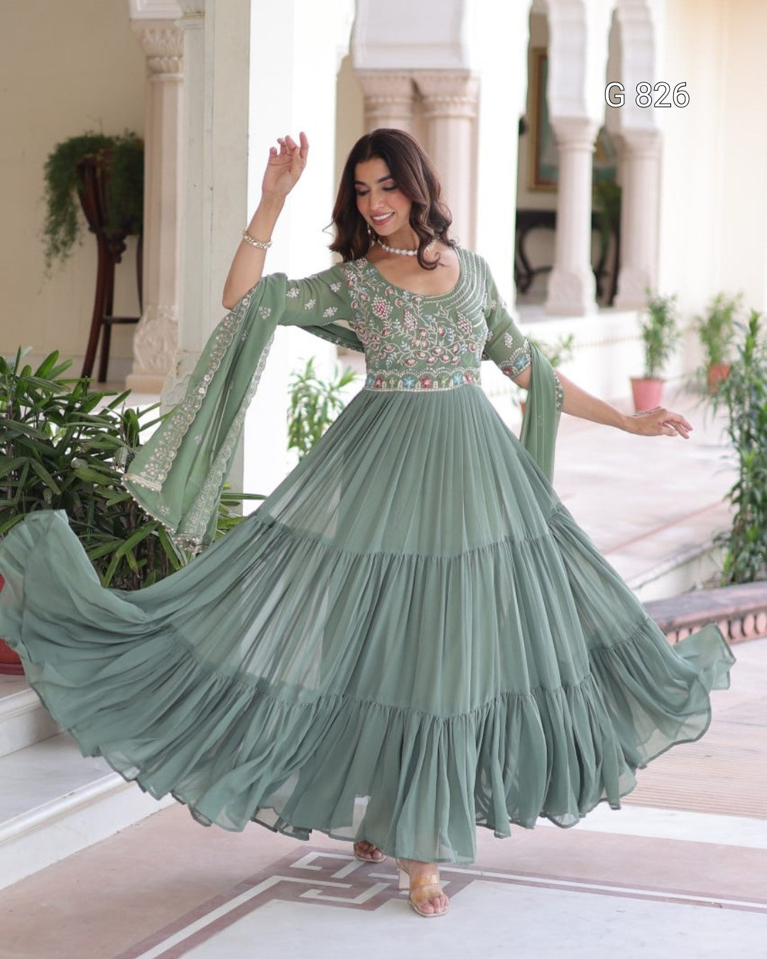 Woman in a long, light green dress with floral patterns in an indoor setting.