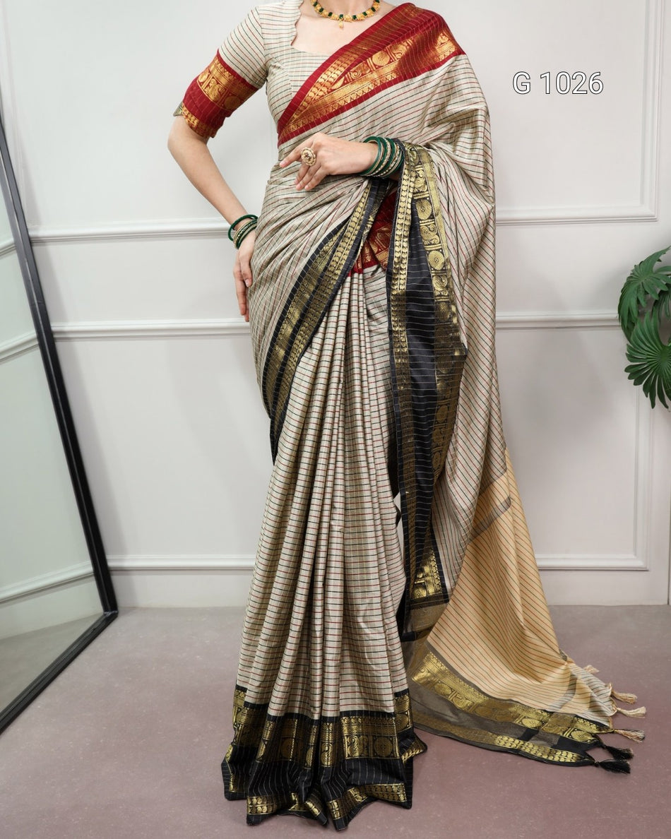 A woman models a traditional Indian saree with a beige and black striped body, a red and gold border, and a beige pallu with gold detailing. She is wearing a red and gold embroidered blouse.