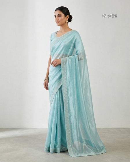 A woman modeling a light blue-green sheer saree with a matching dupatta and border, standing against a plain light gray studio background.