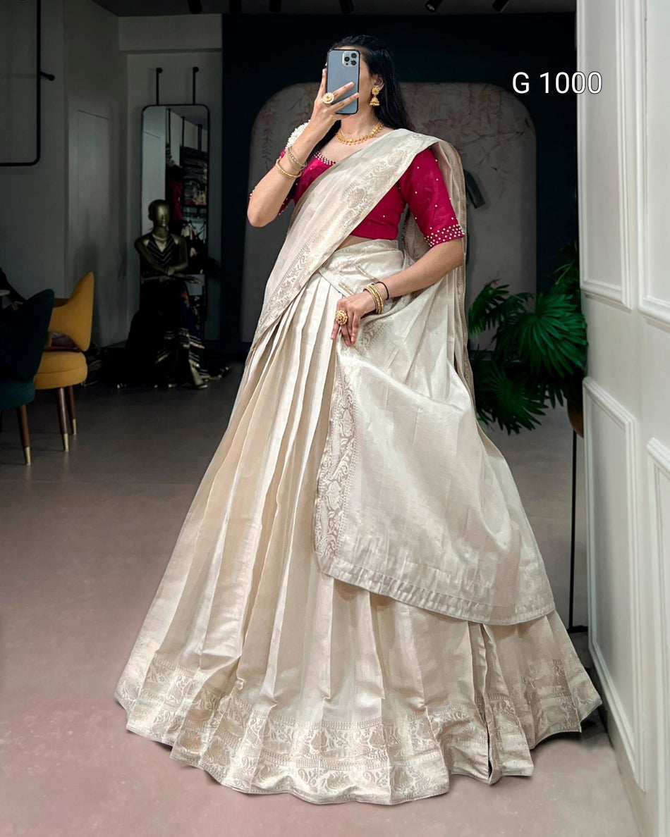 A woman takes a mirror selfie in a boutique wearing a voluminous cream-colored silk saree with a deep red embroidered blouse. The background shows a shop interior with a mannequin, a yellow chair, and a potted plant.