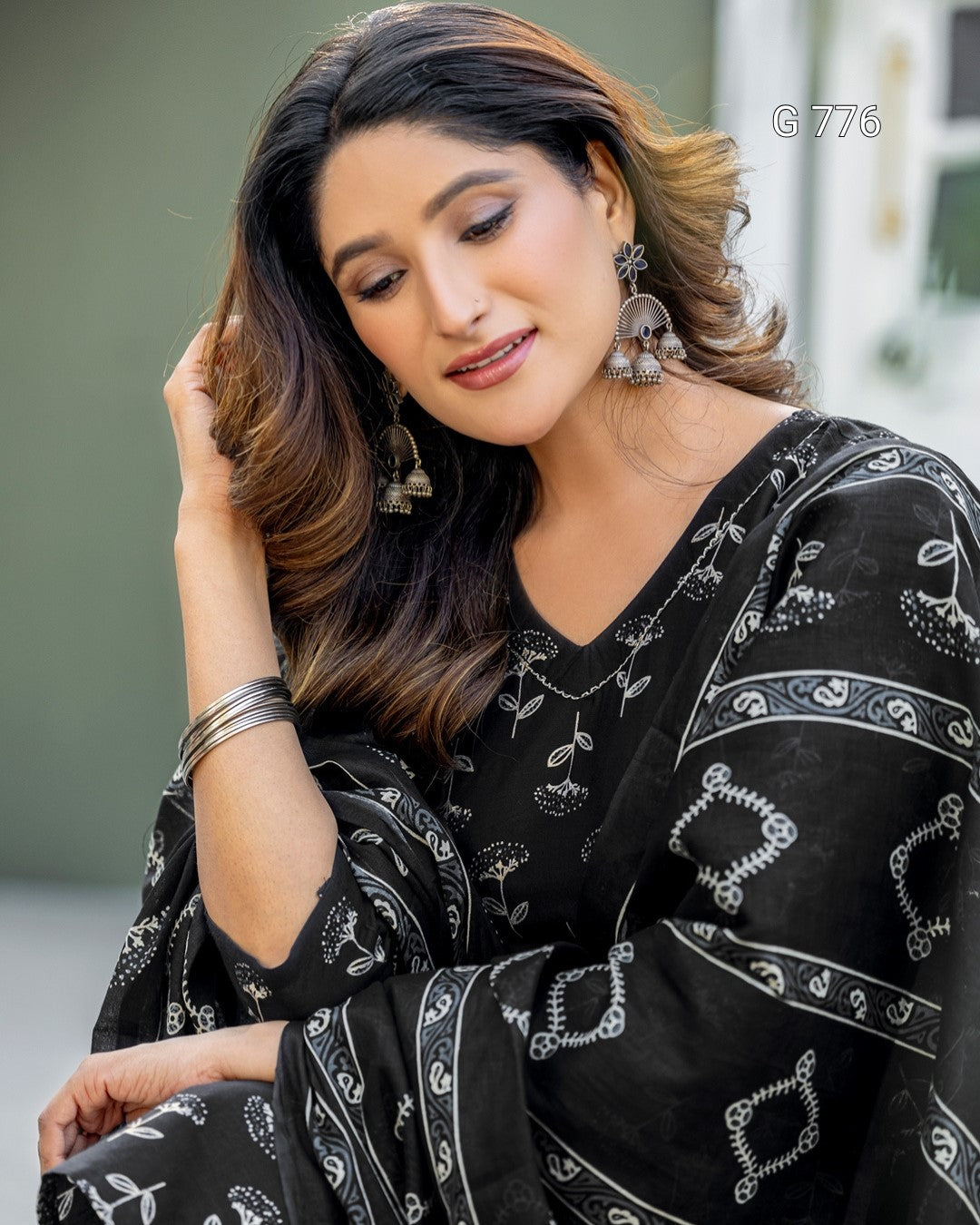 Woman wearing a black saree with white patterns, sitting outdoors.