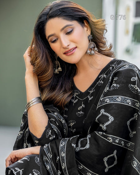 Woman wearing a black saree with white patterns, sitting outdoors.