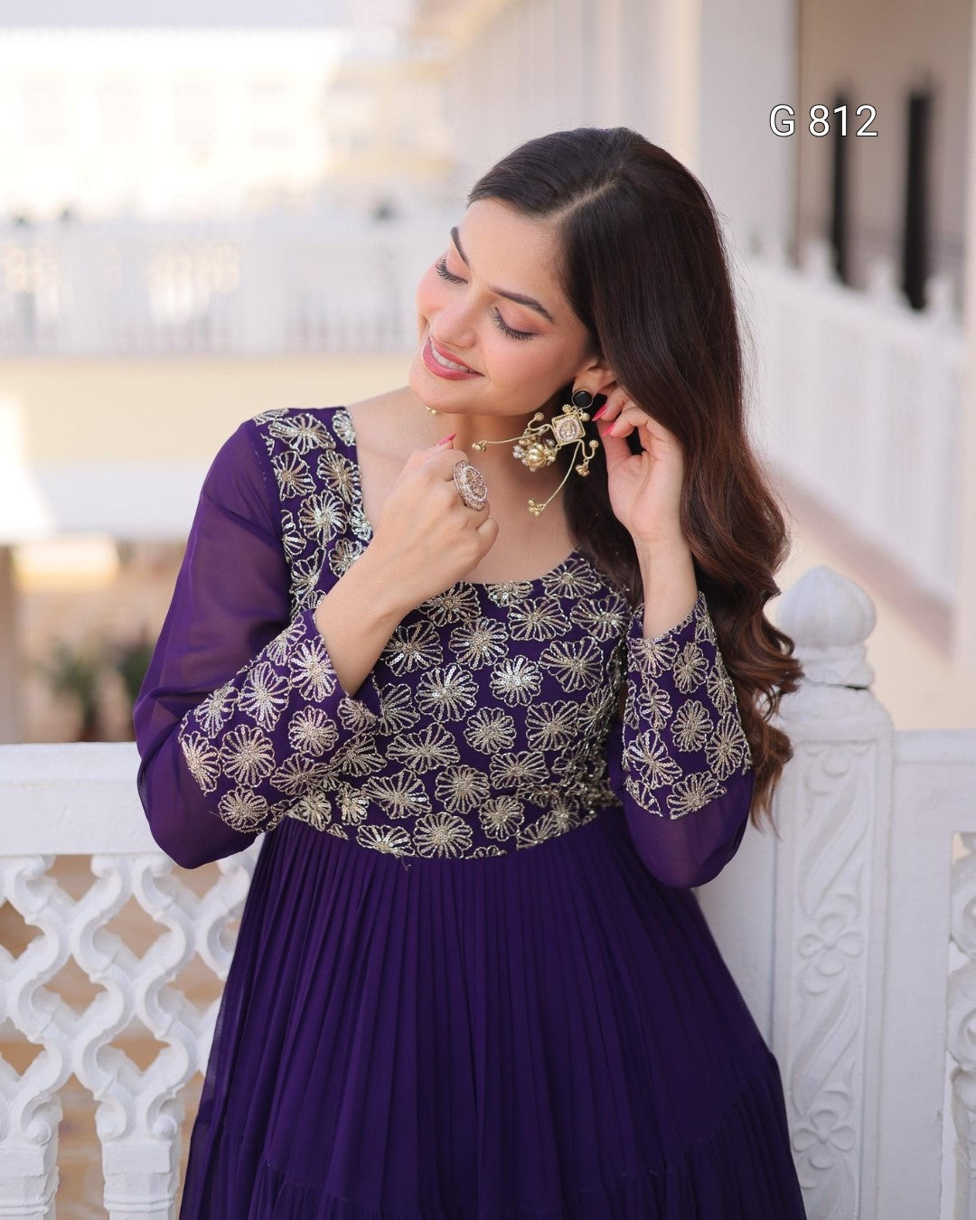 Woman wearing a purple traditional outfit with gold patterns, standing on a balcony.