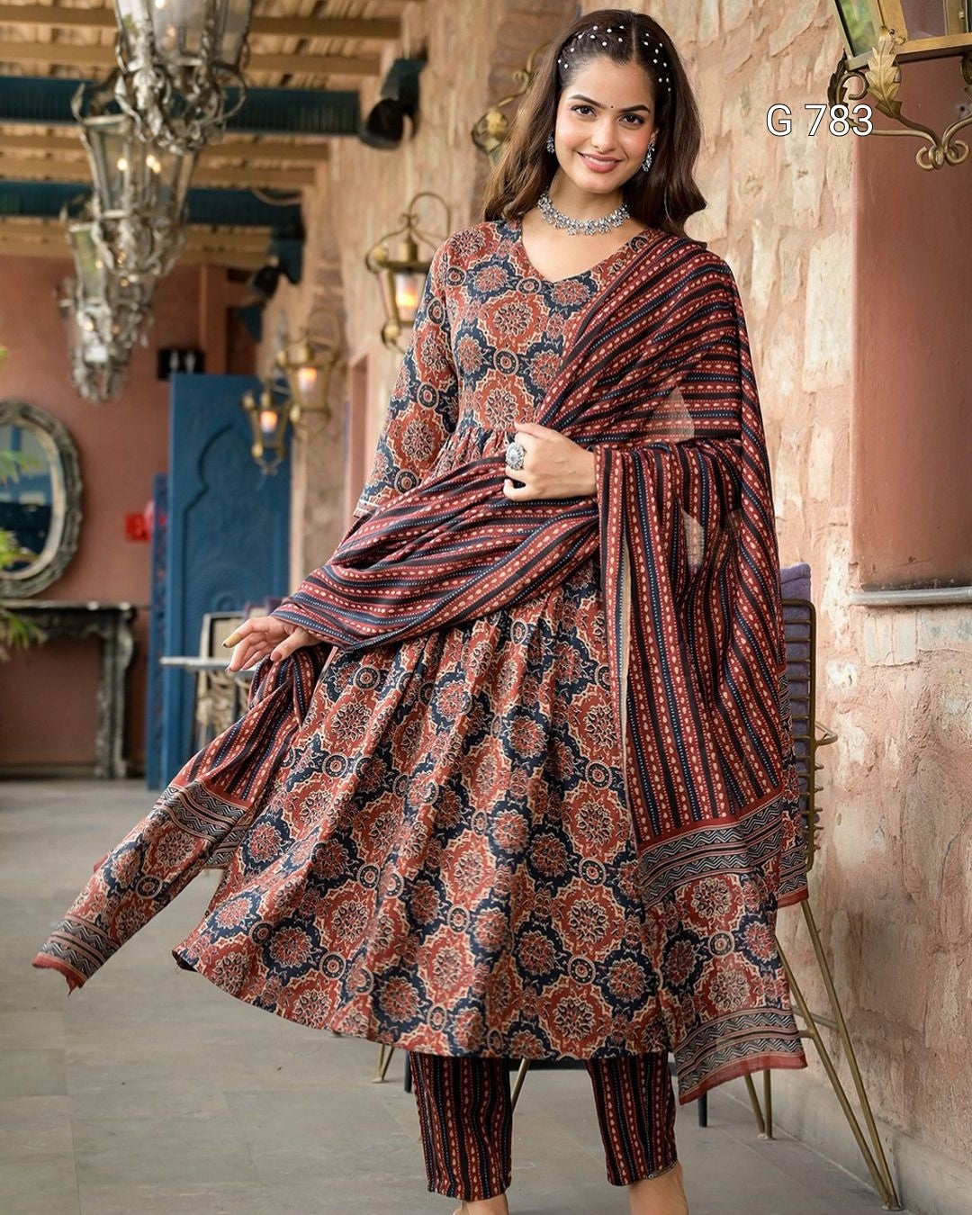 Woman in a patterned traditional outfit standing in an ornate interior setting.