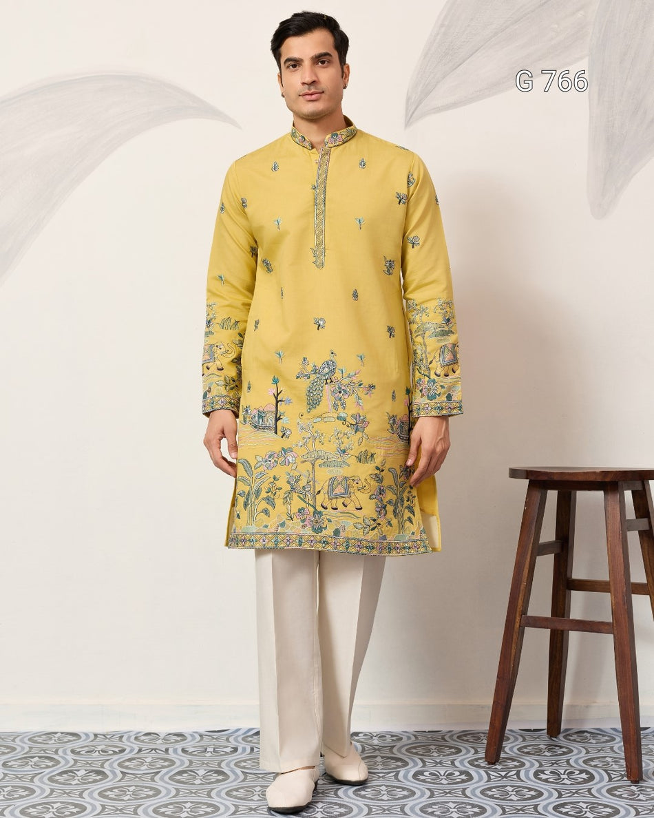 Man wearing a yellow kurta with white pants standing against a light gray background.