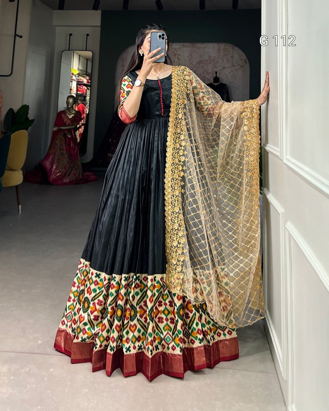 Woman wearing a traditional outfit with a black top and colorful skirt, standing in a room.