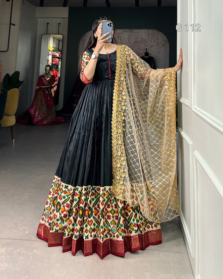 Woman wearing a traditional outfit with a black top and colorful skirt, standing in a room.