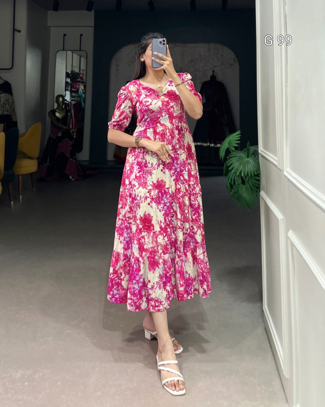 Woman wearing a pink floral dress taking a mirror selfie in a room.