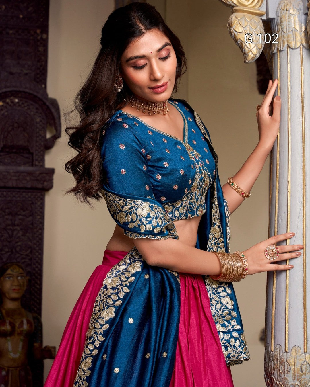 Woman in a traditional blue and pink saree with intricate patterns, standing indoors.