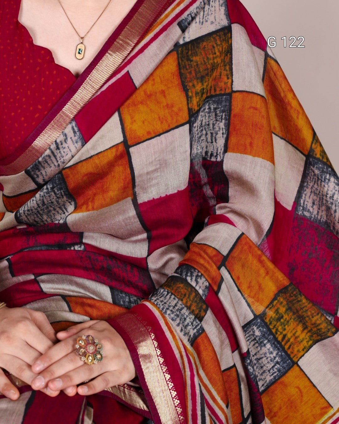 Colorful saree with geometric pattern and a hand wearing a ring, on a plain background.