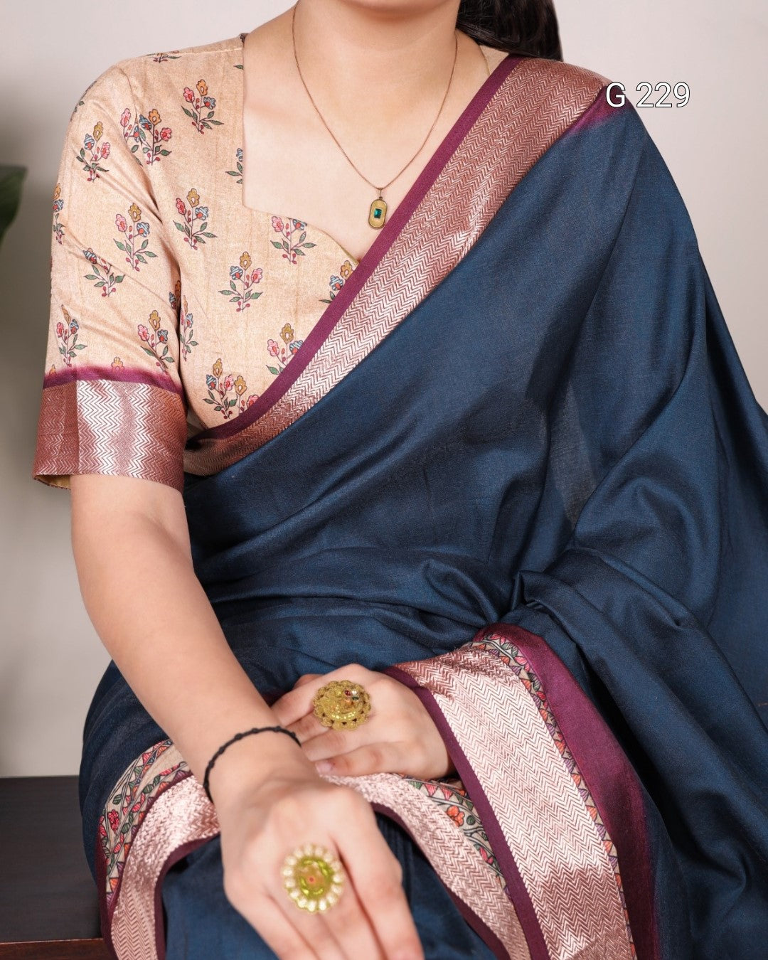 Person wearing a blue saree with floral blouse, sitting indoors.