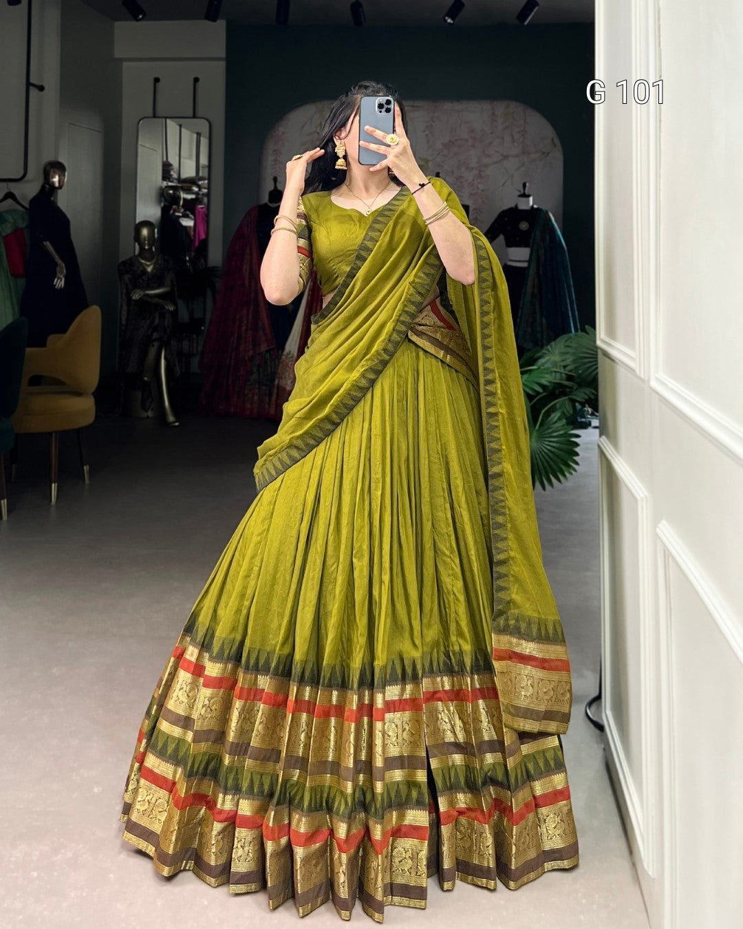 Person wearing a green saree with gold and red patterns in an indoor setting.