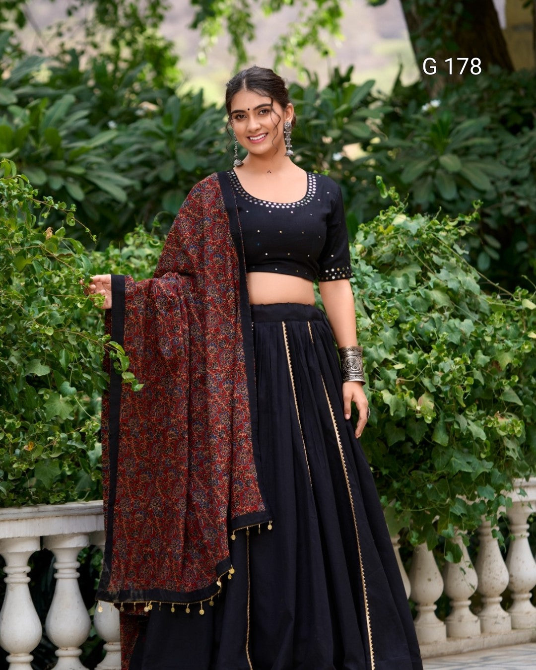 Woman in a black traditional outfit with a patterned shawl against a green outdoor background