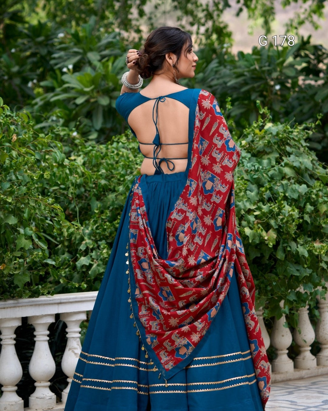 Woman wearing a blue saree with a red and gold patterned shawl, standing outdoors.