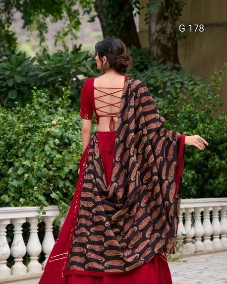 Woman in a red saree with a black and gold patterned shawl, standing outdoors.