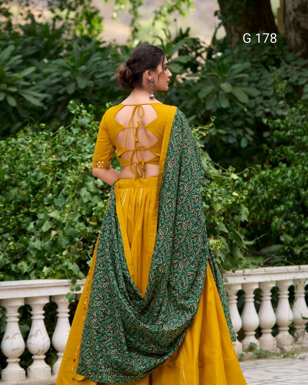 Woman wearing a yellow and green traditional outfit with a floral pattern, standing outdoors.