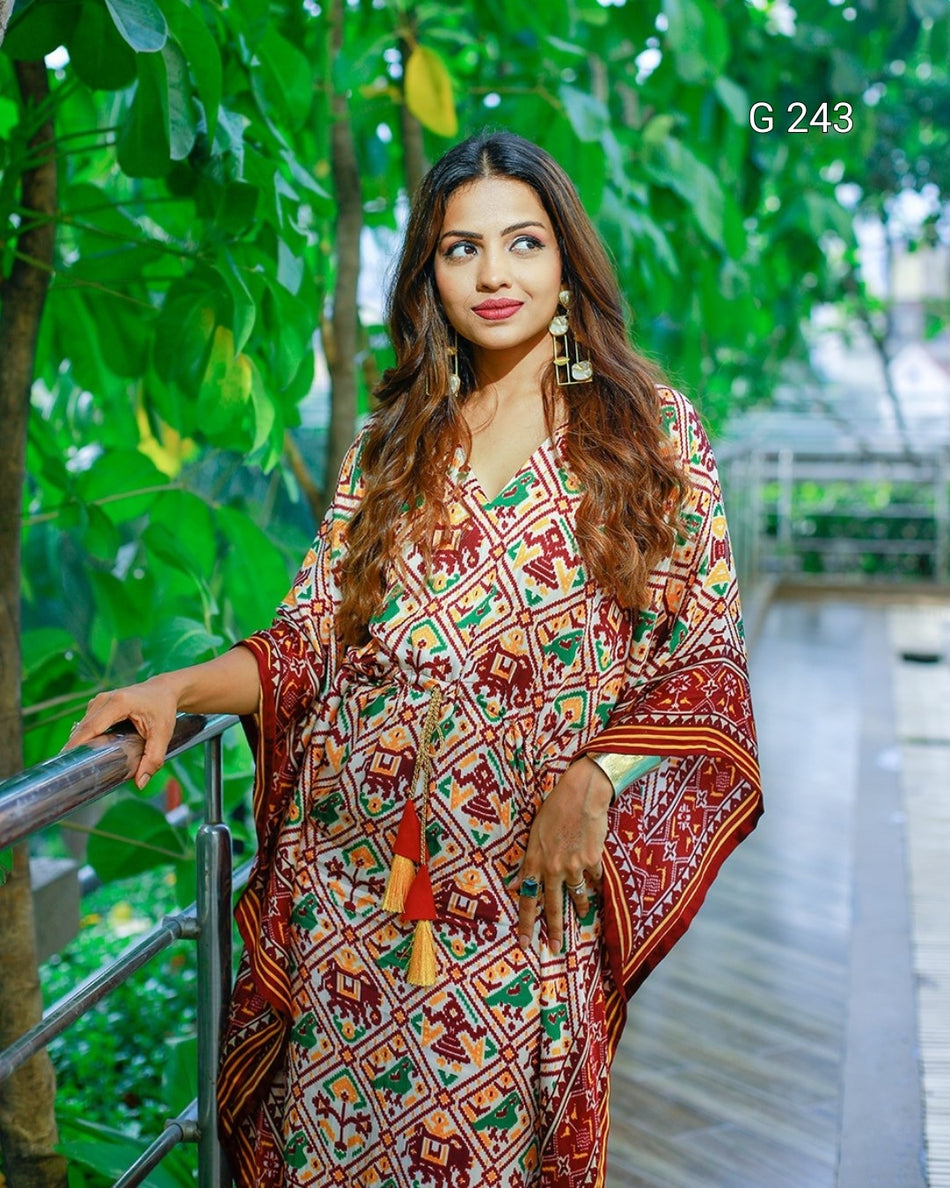 Woman wearing a colorful patterned dress standing outdoors with greenery in the background