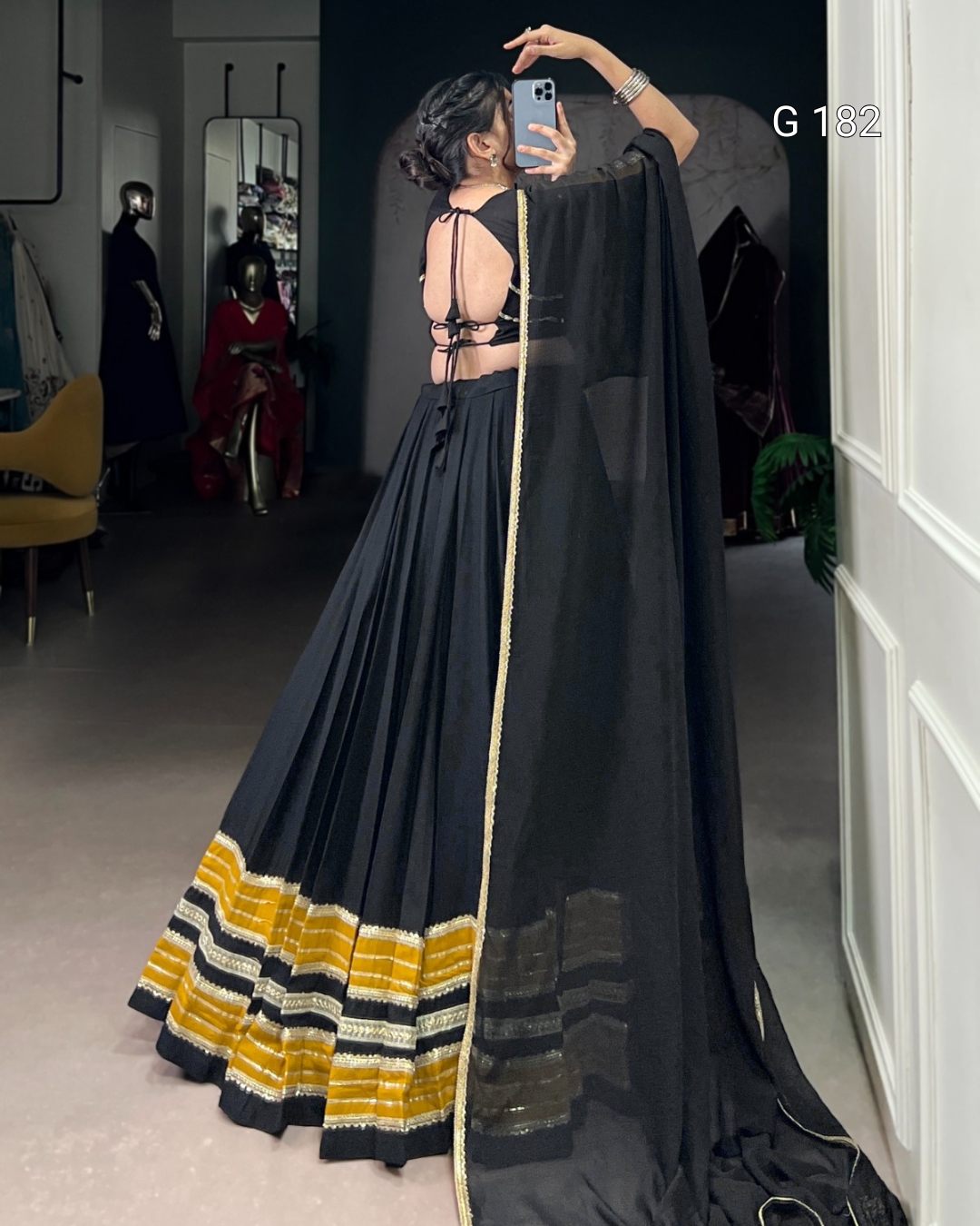 Person wearing a black saree with yellow and white border, standing in a room.