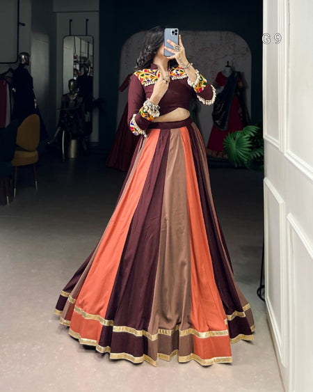 Person wearing a colorful traditional outfit with a patterned top and multicolored skirt in a room.