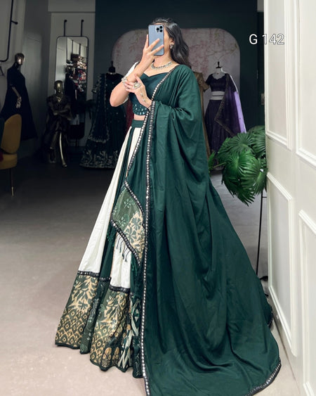 Woman wearing a green and white traditional outfit in a room with mirrors and plants.