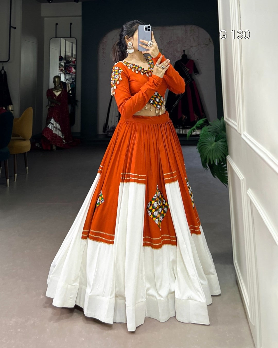 Person wearing an orange and white traditional outfit with embroidery, standing in a room.