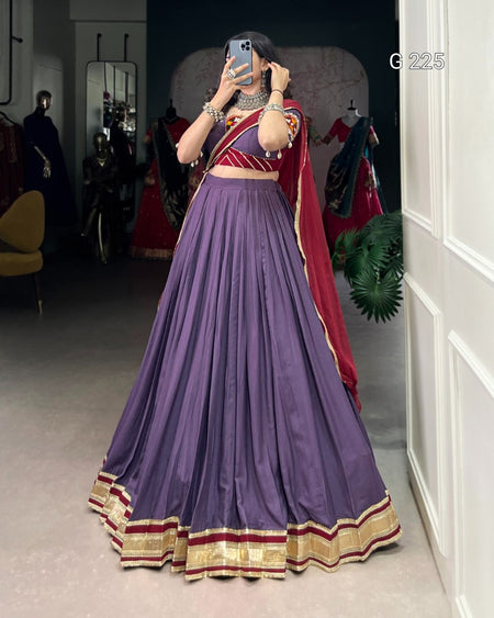 Person wearing a purple saree with red and gold border in a room.